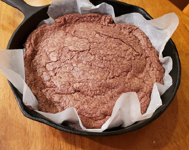 This is a baked chocolate skillet cookie. This is a cookie baked and is cooling in a 10 inch cast iron skillet lined with parchment paper and resting on a oak table