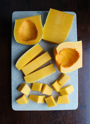 cutting board full of butternut squash pieces in various stages of being cleaned, pealed and diced.