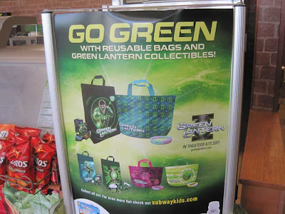 Sign in Subway shop reading Go Green with reusable bags and Green Lantern collectibles!