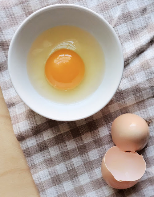 Egg cracked into bowl with eggshells on tea towel