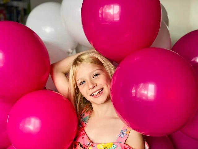 A girl holding a bunch of pink and white self sealing Bunch O Balloons party balloons over her head and smiling