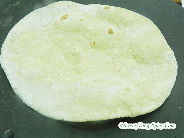 Slightly darker chapatis with small bubbles forming on the surface, indicating the cooking progress on a hot tawa.