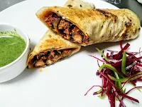 Serving chicken kathi roll in two pieces with green chutney and garnish
