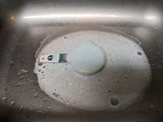 frothing white mixture covering a large area around a measuring cup in a sink