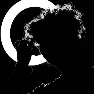Man standing in front of round back light. Curly hair head shot 