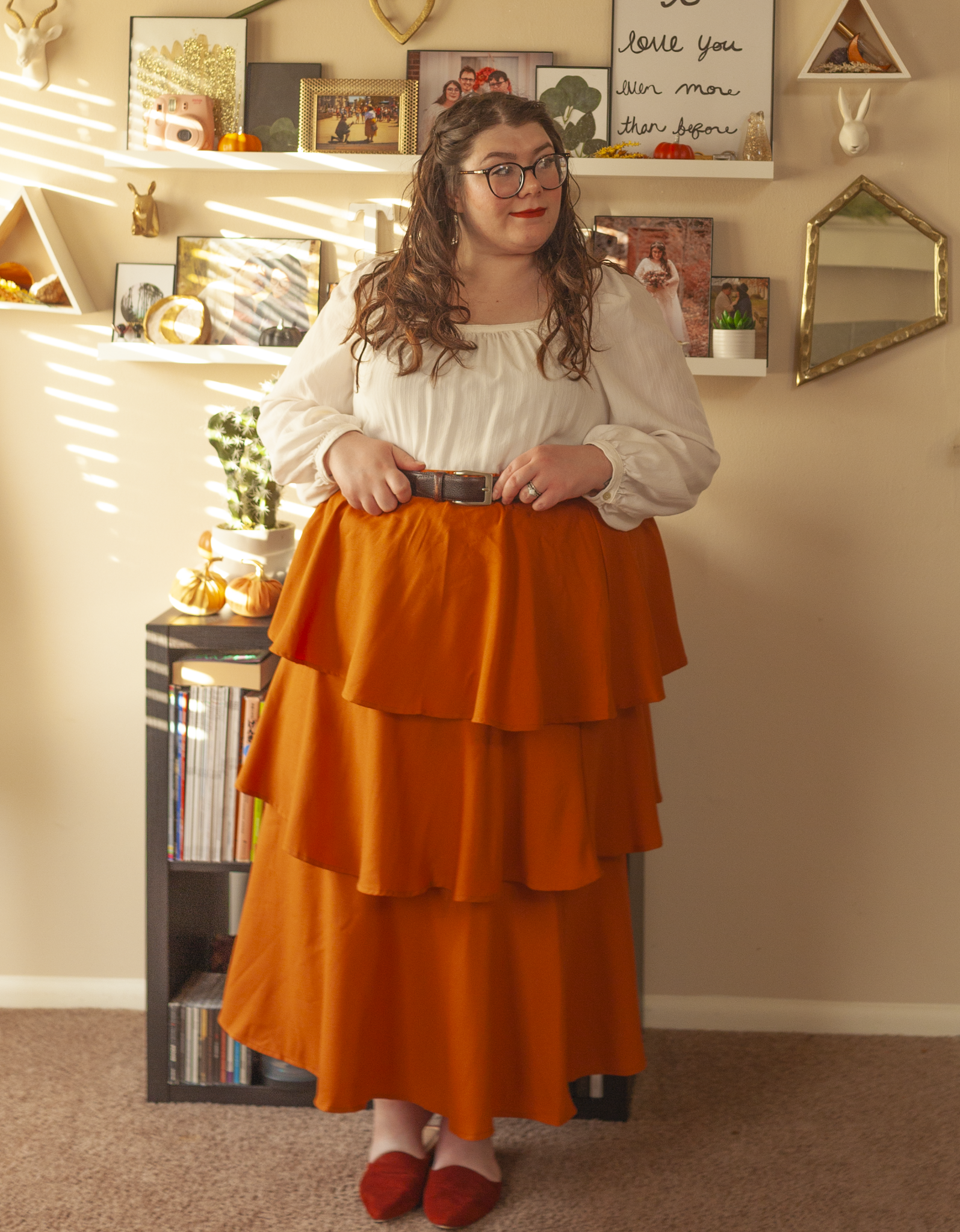 An outfit consisting of a white poet blouse tucked into a tri tiered ginger colored midi skirt and rust colored mules.