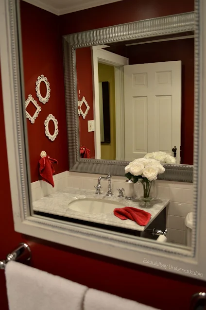 Red bathroom with a silver mirror and white frames hanging on the wall