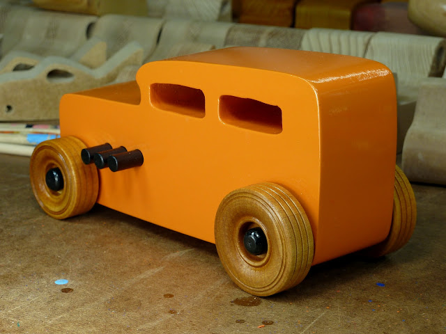 Handmade Wooden Toy Car Hot Rod 1932 Ford Sedan From the Hot Rod Freaky Ford Series Orange & Black Wooden Toys In the Background On Workbench