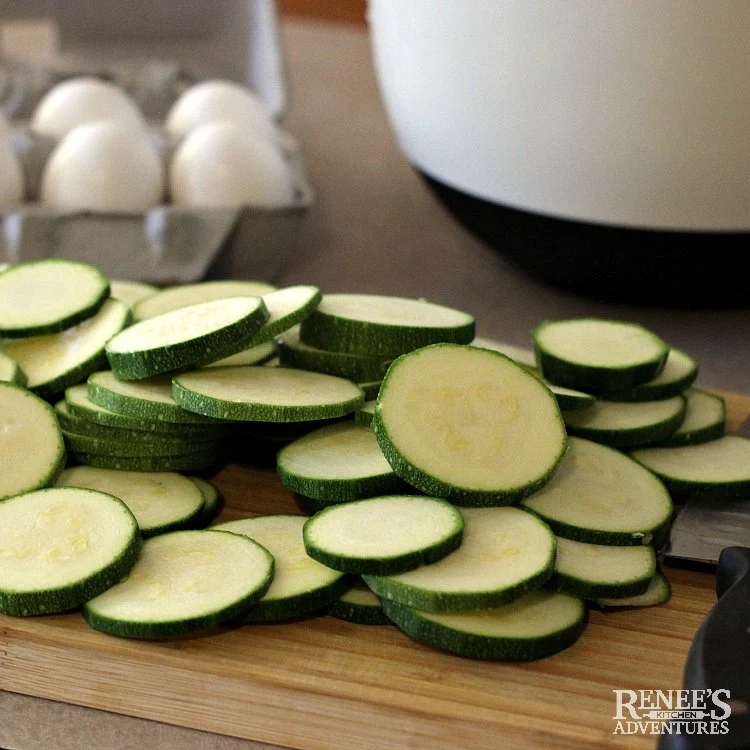 Prepping for zucchini appetizer with sliced zucchini on cutting board and carton of eggs in background