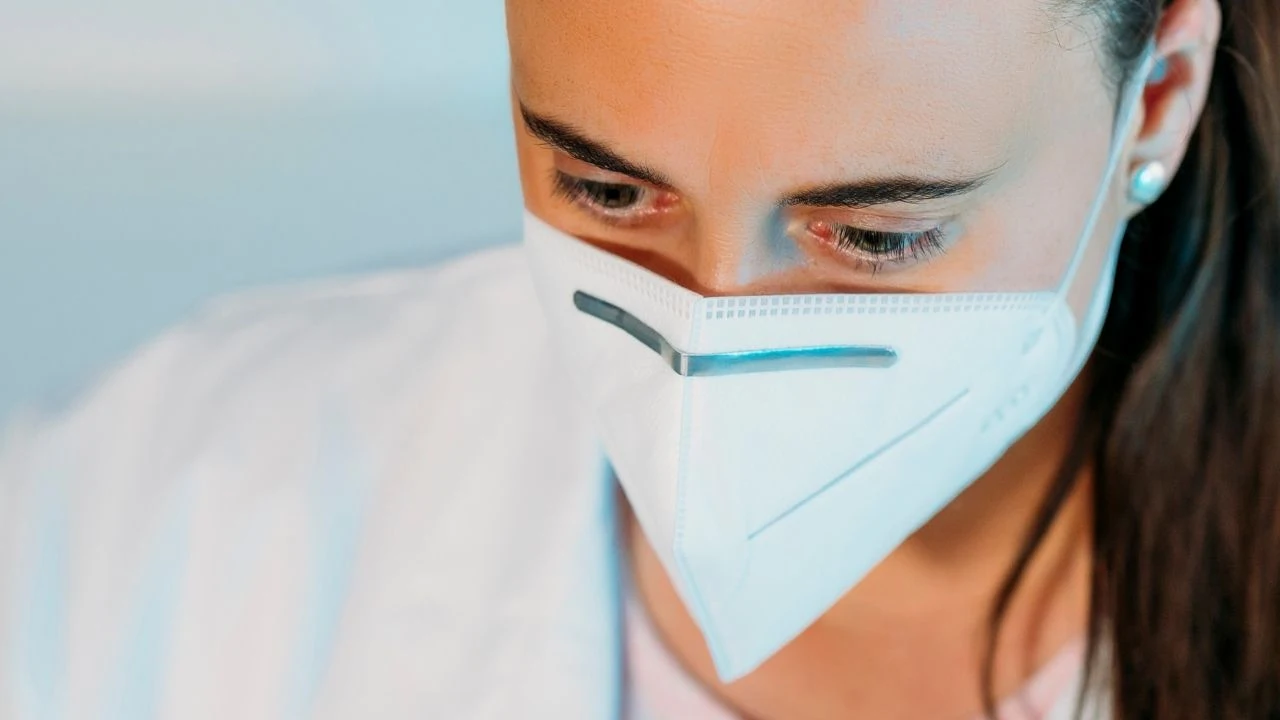 Young woman doctor wearing white coat and protection face mask against coronavirus at workplace.