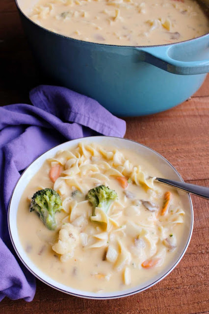 This cheese soup is a copycat recipe my family has enjoyed for years. It is full of vegetables, pasta and creamy cheesy goodness. It's a regional favorite and soon to be a favorite for you as well! bowl of soup next to a pot of chunky cheese soup