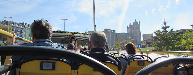 Pessoas sentadas no andar superiro do autocarro panorâmico e a Catedral do Porto ao fundo
