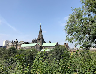 a photo showing a view of Glasgow Cathedral from the Necropolis.  The cathedral is in a half frame of trees growing in and around the Necropolis.  Photo by Kevin Nosferatu for The Skulferatu Project.