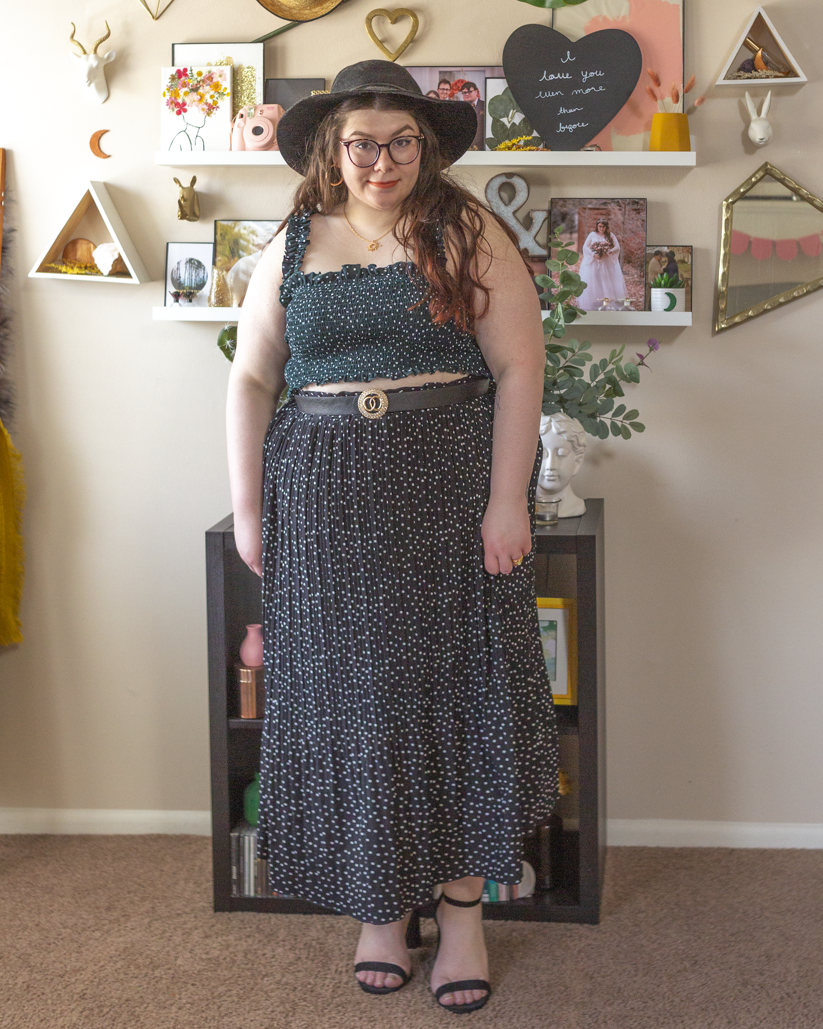 An outfit consisting of a white on black swiss dot ruffled shirred crop top tank and white on black swiss dot pleated midi skirt and black strappy sandal heels.