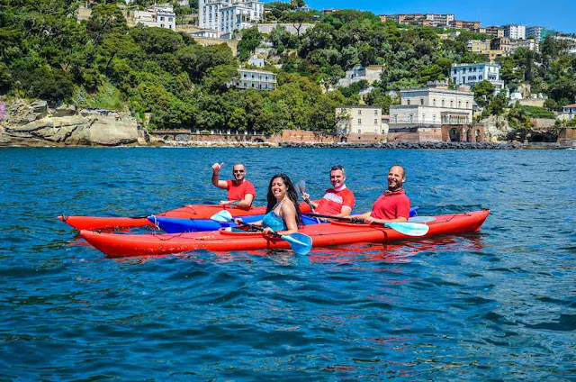 four people say cheese to the photographer during a kayak excursion in the bay of Napoli souther Italy