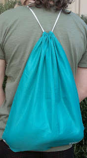 Promotional drawstring backpack on someone's back, showing how the nylon cord of the drawstring loops over the shoulders, down the side and through the eyelets at the bottom of the bag.
