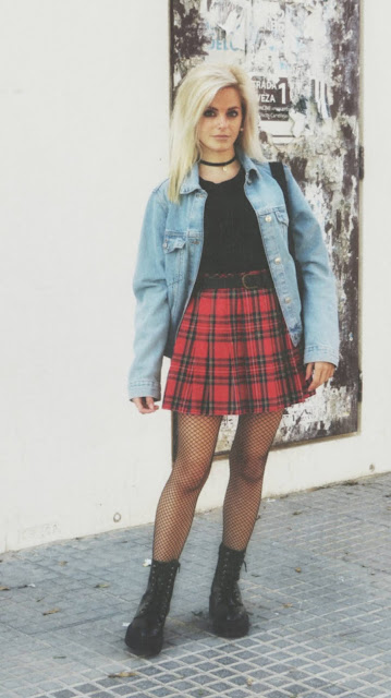 Estilo grunge con camiseta negra, falda de tablas tartán, medias de red grande, botas estilo militar y cazadora vaquera
