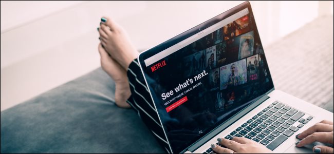 تمدد أقدام امرأة على كرسي قدم وهي تتصفح Netflix على جهاز كمبيوتر محمول.