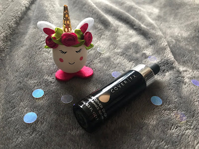 a bottle of foundation on a grey blanket next to a egg shaped unicorn toy