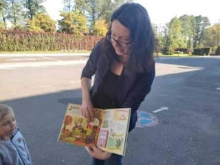 Pani bibliotekarka stoi i pokazuje dzieciom książkę.
