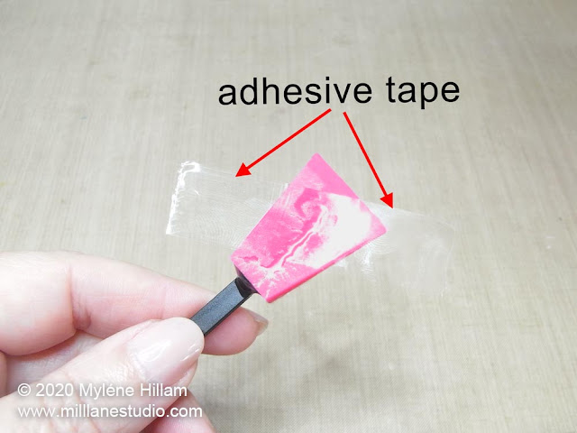 A hand holding a silicone stirrer with a piece of adhesive tape pressed across the silicone