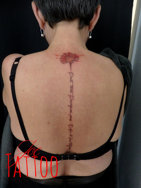 une phrase avec beaucoup de sens tatouée sur la colonne vertébrale ornée d'une fleur de gerbera rouge orangés