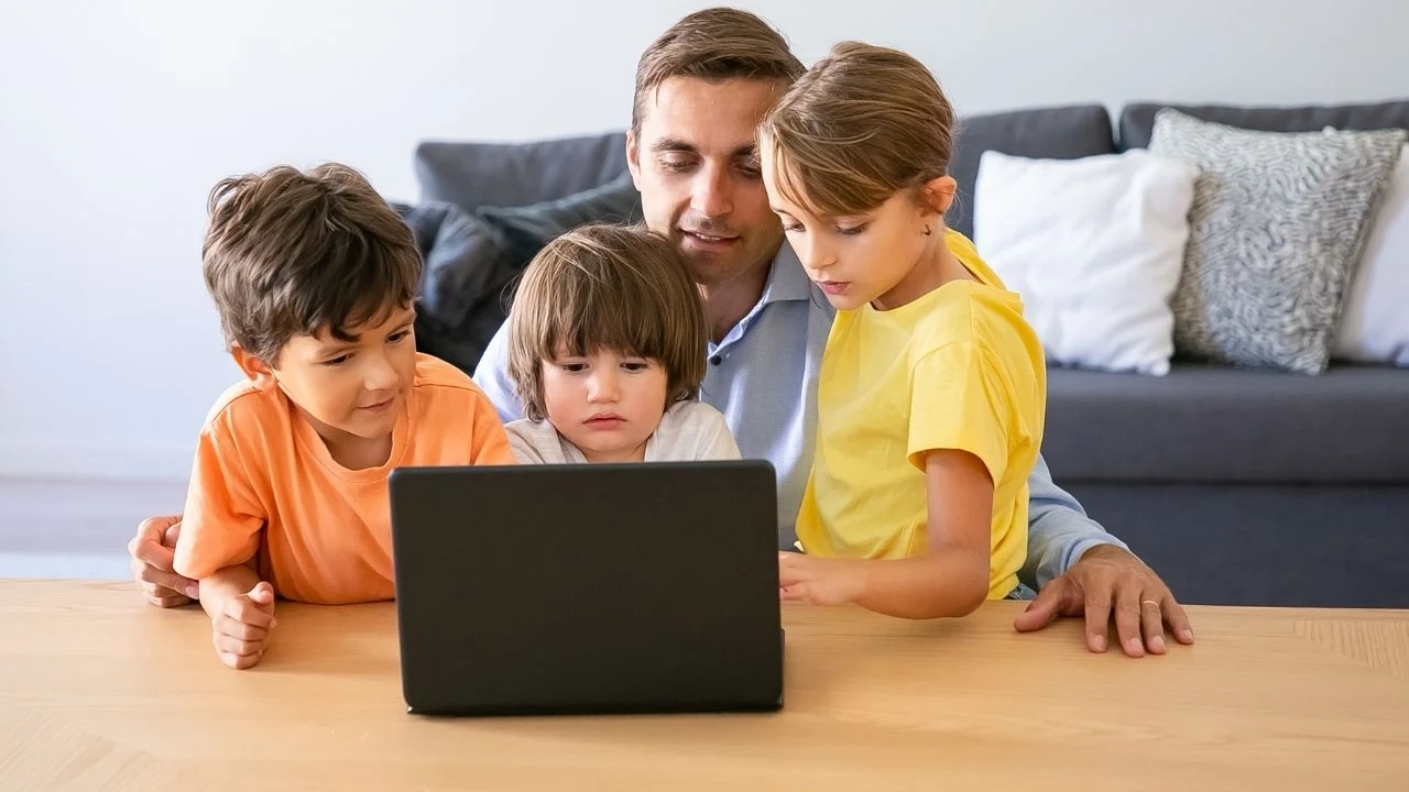 Caucasian dad wathcing movie via laptop with kids. Happy father sitting at table with lovely children.