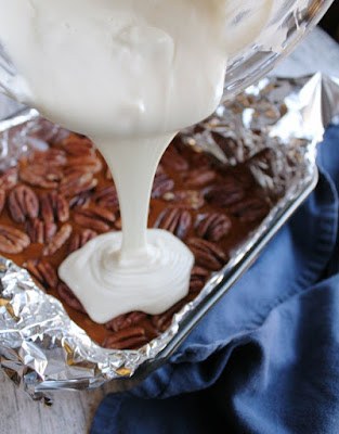 pouring melted white chocolate over caramel and pecans