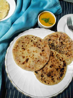 Serving onion kulcha in a plate, dal and papad in background