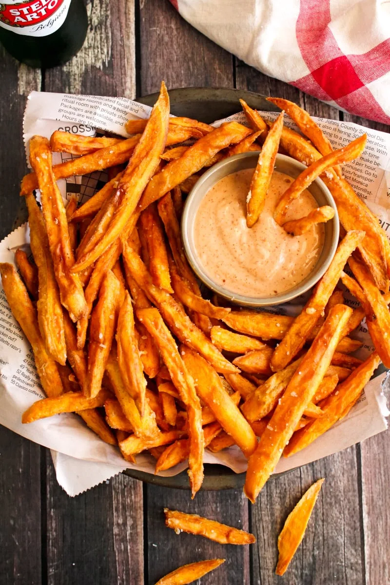 Top view of sweet potato fries on a pie plate lined with newspaper on a wood background.