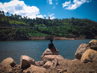 Little Boy Sitting On A Boulder Enjoy The Natural Atmosphere On The Edge Of Lake Water Dam Titab Ularan North Bali Indonesia