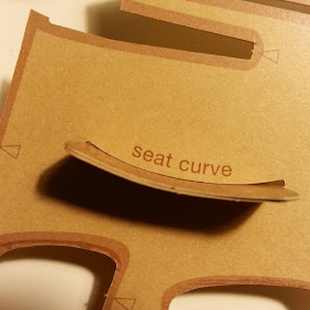 Piece of cardboard threaded through a curved slit marked 'seat curve'.