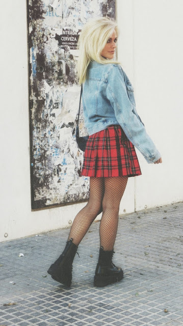 Estilo grunge con camiseta negra, falda de tablas tartán, medias de red grande, botas estilo militar y cazadora vaquera