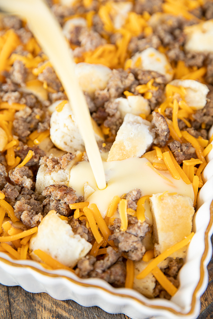 Sausage Biscuit Breakfast Casserole - only 5 ingredients! Frozen buttermilk biscuits, sausage, cheddar cheese, eggs, and milk. Can make in advance and refrigerate or freeze for later. Great for breakfast, lunch, or dinner. I took this to a potluck and it was the first thing to go! Make it ASAP! #breakfast #casserole #sausage #biscuits #freezermeal egg and milk being poured in baking dish