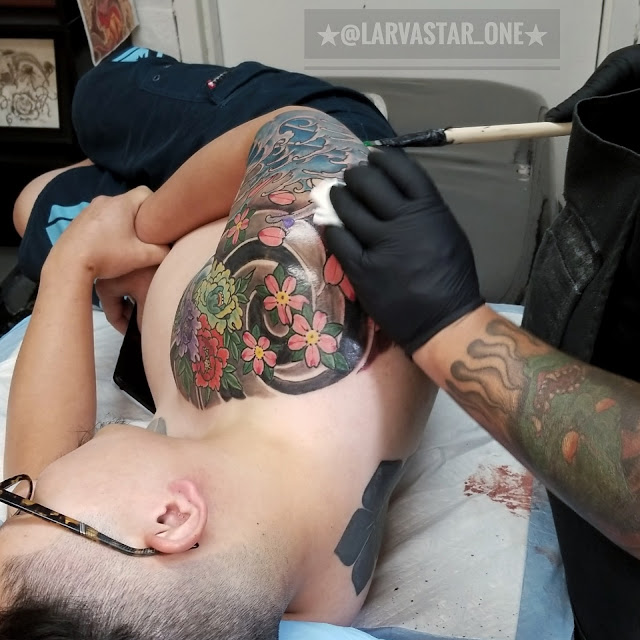 man laid on his left side getting a Cherrie blossom tattoo with blue waves done on traditional tebori tattoo style at zero one ink Sacramento  California