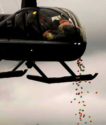 Black helicopter with people inside dropping colorful plastic eggs into the air below