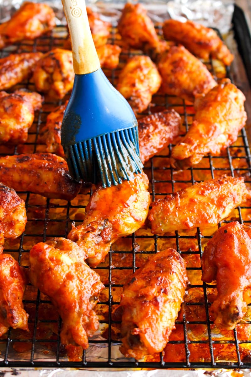 Side view of Baked Buffalo Chicken Wings being basted with buffalo sauce.