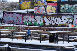 A lady walks her dog in the snow past the grafitti