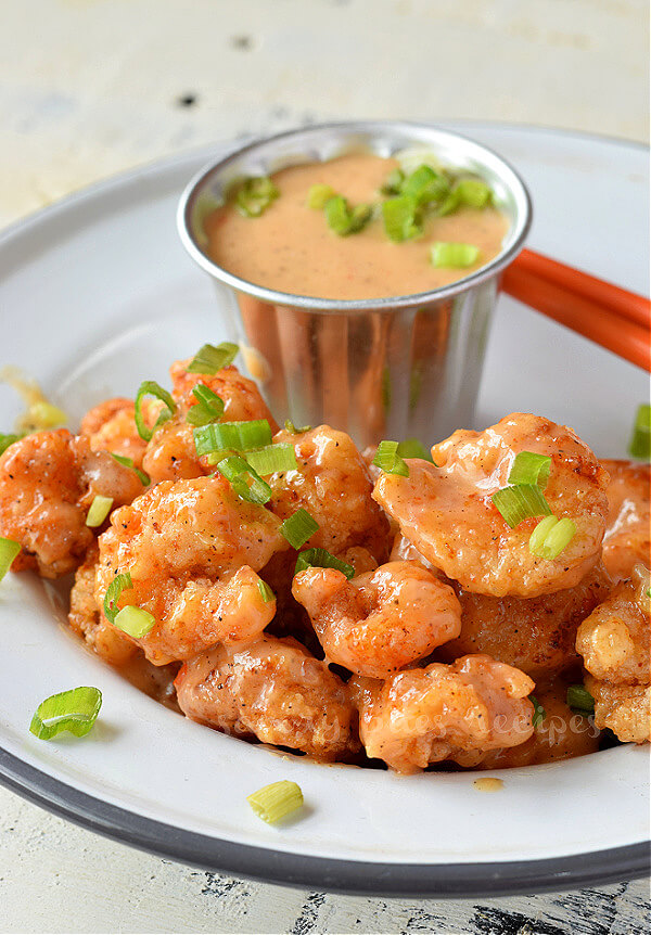 Try this quick,easy and best copycat bonefish grill bang bang shrimp recipe with amazing bang bang sauce. The shrimp are crispy fried or for a healthy option air fry them or bake further toss them in sweet and savory sauce.You can serve this with rice,or with pasta,in rice bowl or in Asian salad. #savorybitesrecipes #bangbangshrimp #bonefishgrill #appetizer #recipe #shrimp #copycatrecipe a close look of a white plate with crispy bang bang shrimp topped with chopped spring onion