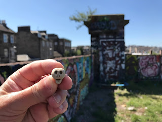 Skulferatu #41 - a small, clay skull being held up with a view of the remains of the Leith Walk Railway Bridge in the background.  Photo by Kevin Nosferatu for the Skulferatu Project