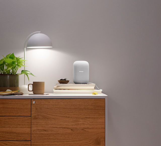 A Nest Audio device sits on a side table next to a lamp and a cup of coffee