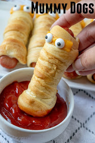 Crescent roll wrapped hot dog with eyes dipping into a small bowl of ketchup
