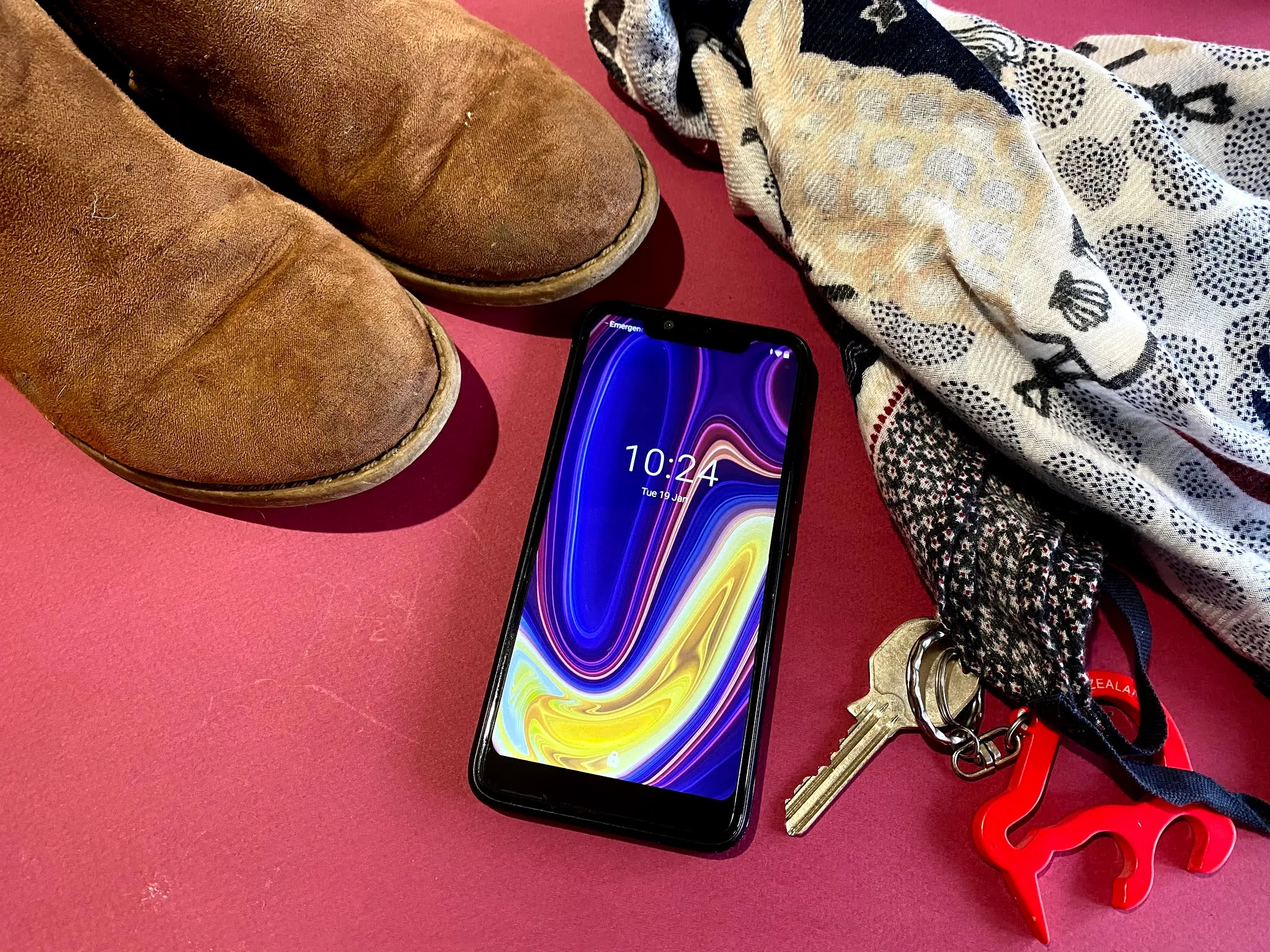 A cheap smartphone mobile next to a scarf, tween boots and keys