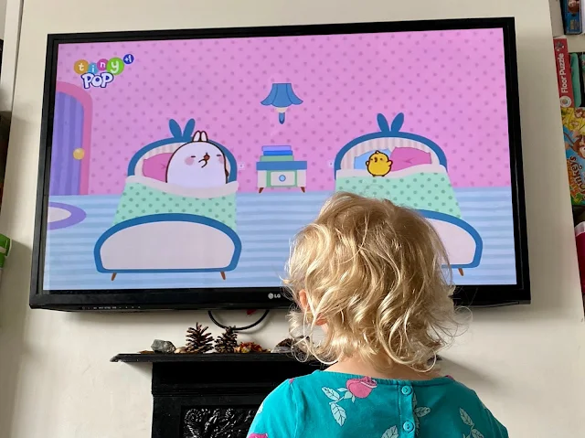 A photo of the back of a young girls head as she looks towards a TV with an episode of Molang on it