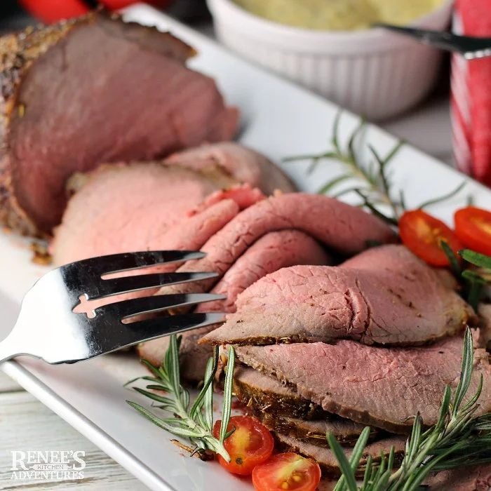 Eye of round Roast sliced on white platter and garnished with fresh rosemary and grape tomatoes