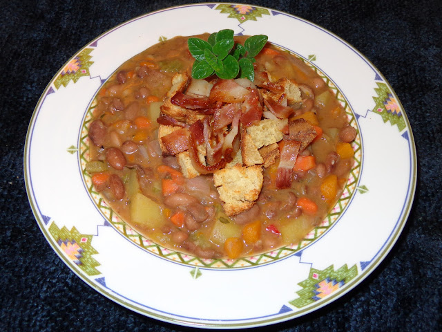 PORTIONS: 4 INGREDIENTS 12 oz. / 340 g dried pinto beans 6 cups chicken broth or water with 1 chicken bouillon without MSG 1 tsp. salt 5 slices thick bacon 1 cup red onions, diced 2 garlic cloves, minced 1 celery rib, diced ½ yellow pepper, diced ½ orange pepper, diced ½ cup red pepper, diced 1 large carrot, diced 1 cup butternut squash, diced 1 potato, diced with or without skin 2 tsp. fresh thyme leaves 3 tsp. fresh oregano leaves ¼ tsp ground pepper ½ cup croutons METHOD Check the beans for stones o any foreign objects in it. Place the beans in a pot covered with plenty water and let it soak for about 8 hours or overnight. Discard the water and fill with 6 cups of fresh water and salt. Bring it to a boil and with a ladle remove the foam from the top. Reduce the heat to simmer, cover and cook the beans for about 1 hour or until beans are very soft. Cook the bacon in a frying pan at low heat. Cook it the way you like it and set aside. Using same frying pan with the bacon fat, add garlic and onions and cook until transparent. Add and slightly brown the vegetables, scraping the bottom of the pan to lose the bacon particles. Incorporate the vegetables to the beans. Using some of the water of the beans deglaze the frying pan and add it to the beans. Add potato, herbs, water, chicken bouillon and pepper. Bring it to a boil, reduce heat, cover and let it simmer for about 15 minutes until potato is cook. Cut the bacon in small pieces. Serve the soup with croutons and bacon.  