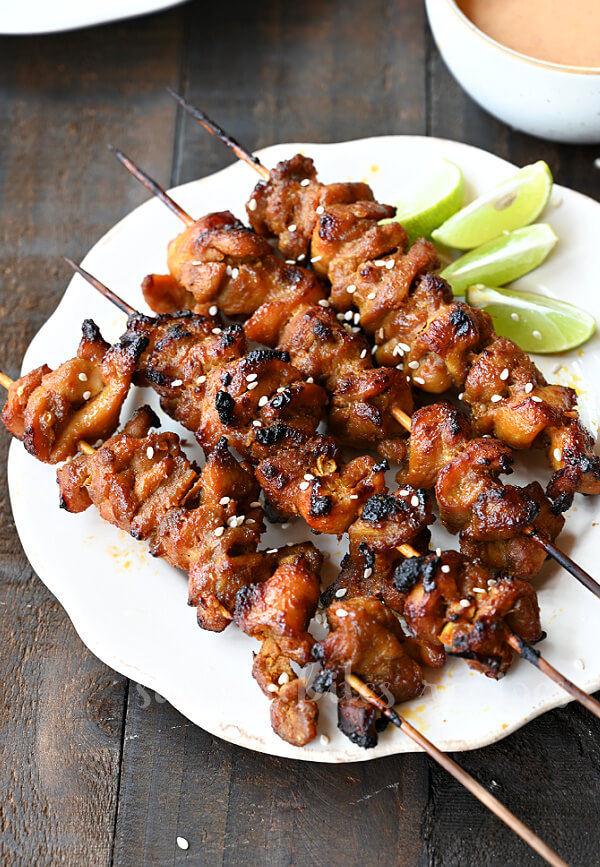 a white plate with grilled Thai coconut chicken skewers