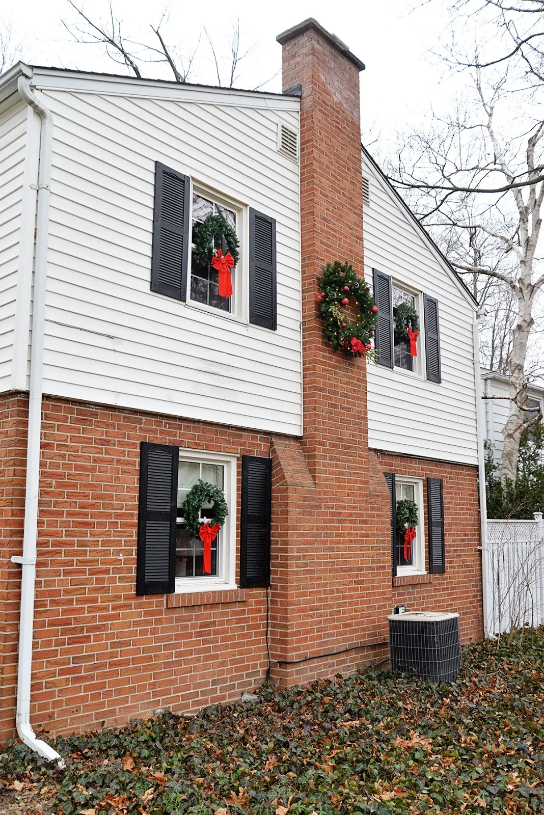 Christmas colonial house with wreaths with candles in windows. Large wreath on chimney.