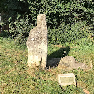 A picture showing both the Hob Stone and The Plague Stone on Little Hob Moor in York.  These two weather worn stones stand on a grassy verge with trees and bushes in the background.  Photo by Kevin Nosferatu for the Skulferatu Project.