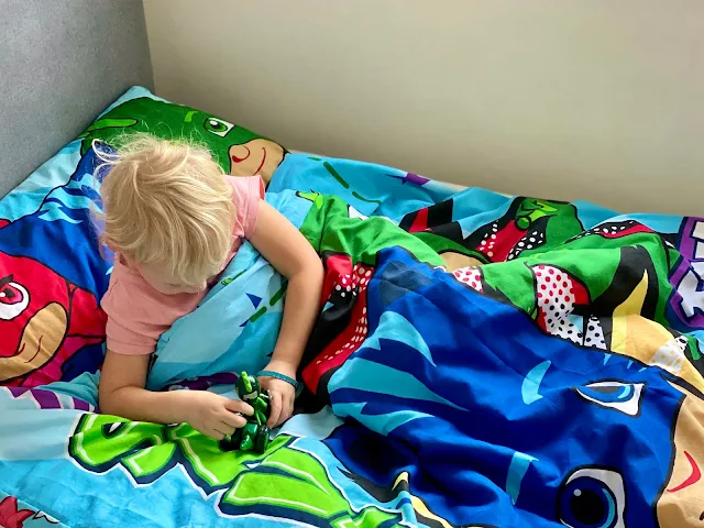 Child in a bed with PJ Masks duvet and pillow cover playing with a gecko toy